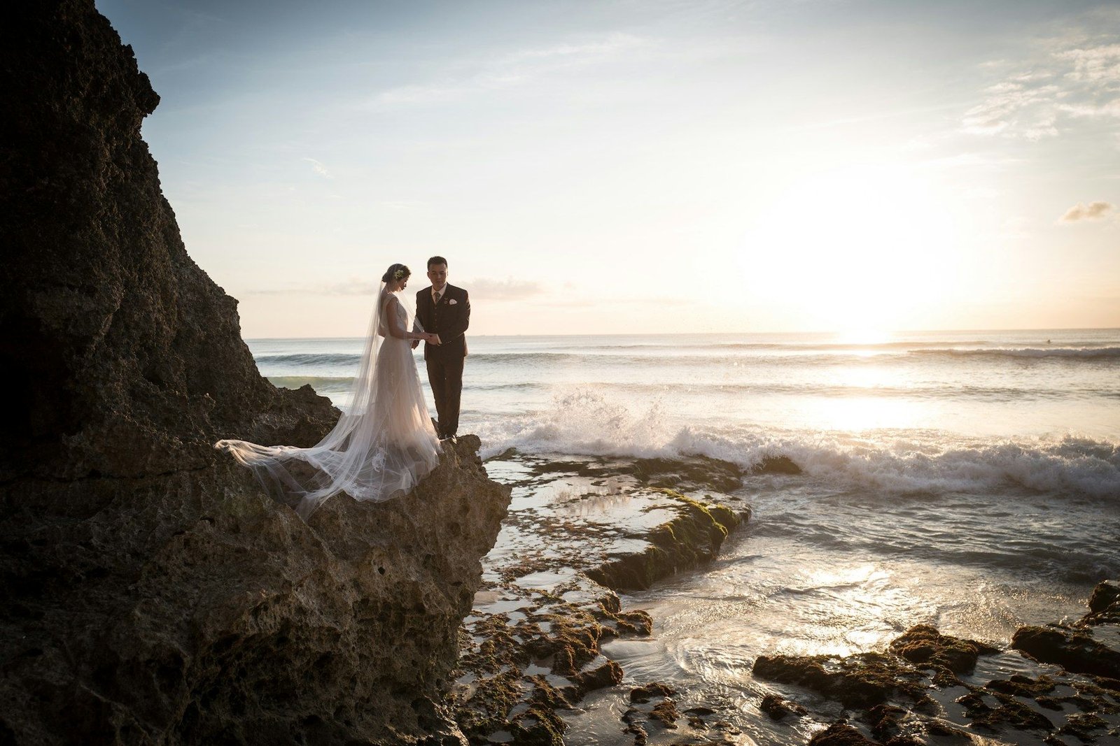 Bride and groom on a cliff above the ocean at sunset